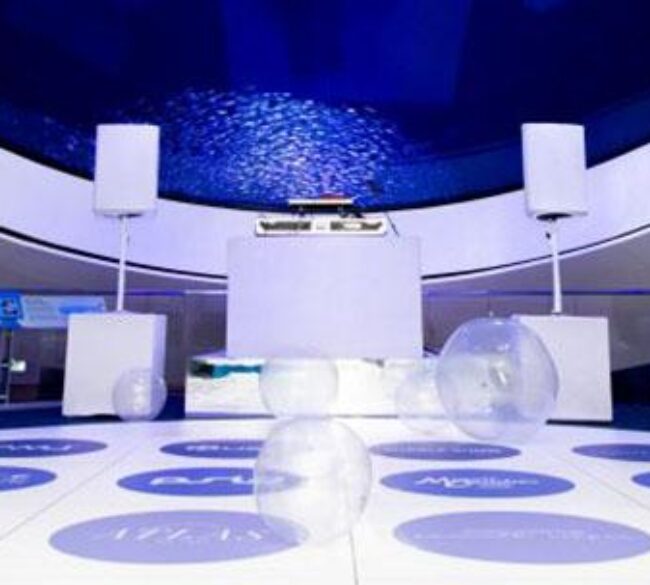 Dance floor image with giant plastic bubbles on it. The room and floor are white with blue lights.