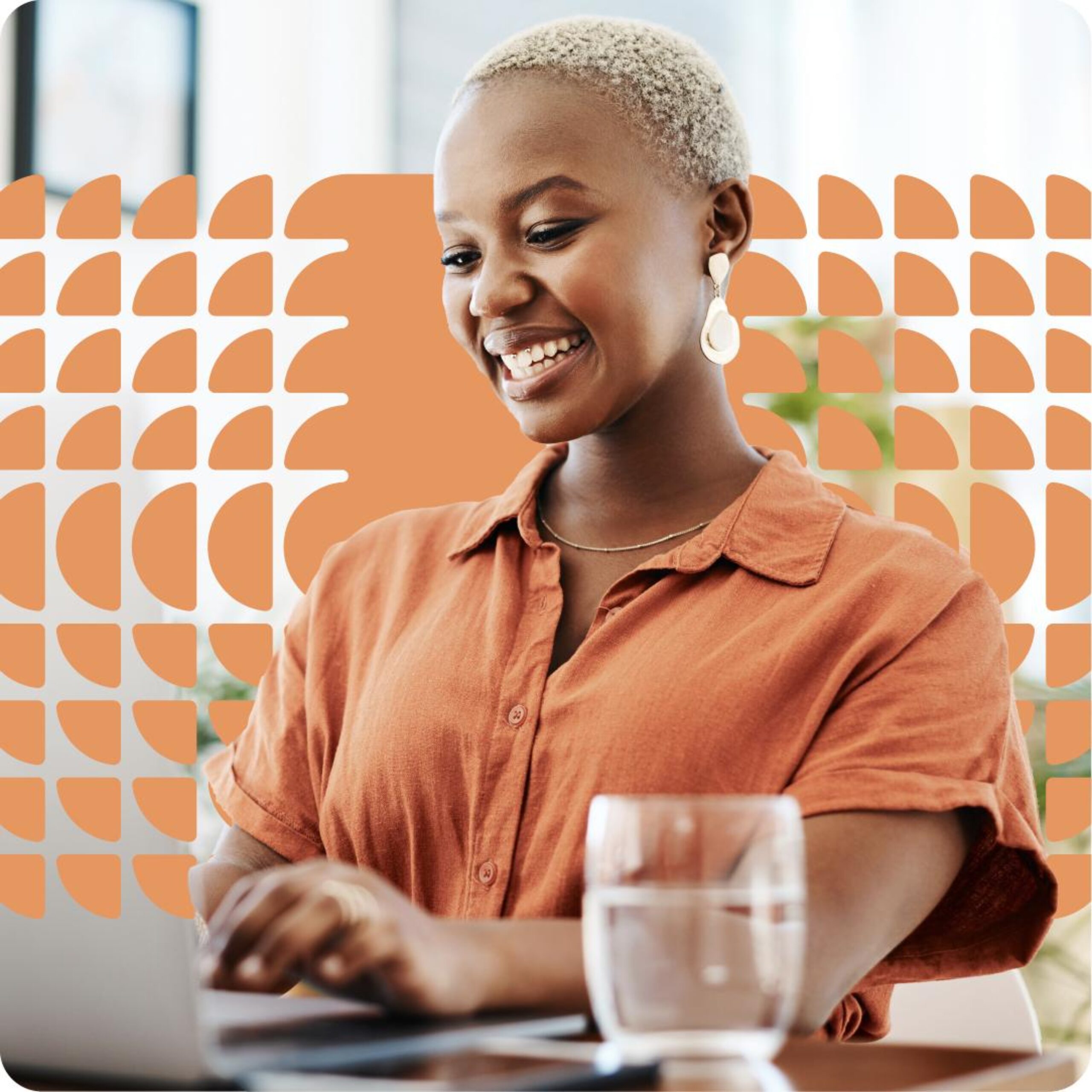 A person with short hair smiles while typing on a laptop, with a glass of water in the foreground and an orange geometric pattern in the background, possibly working on some 3D event diagramming.