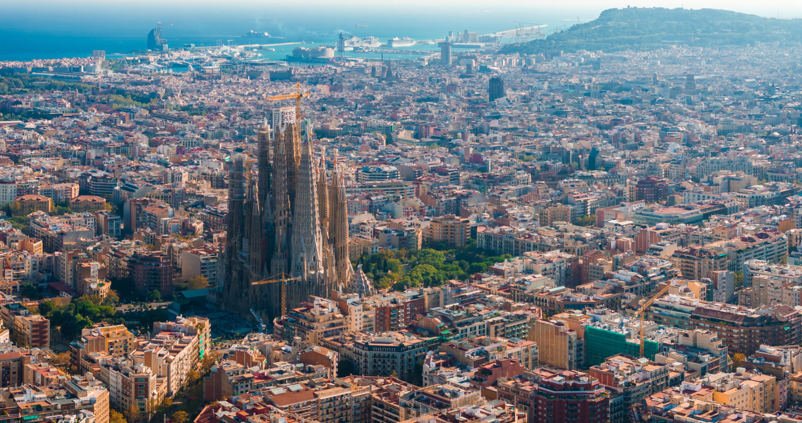 Background image. It's a photo of an aerial view of the Barcelona City Skyline and the Sagrada Familia Cathedral at sunset.