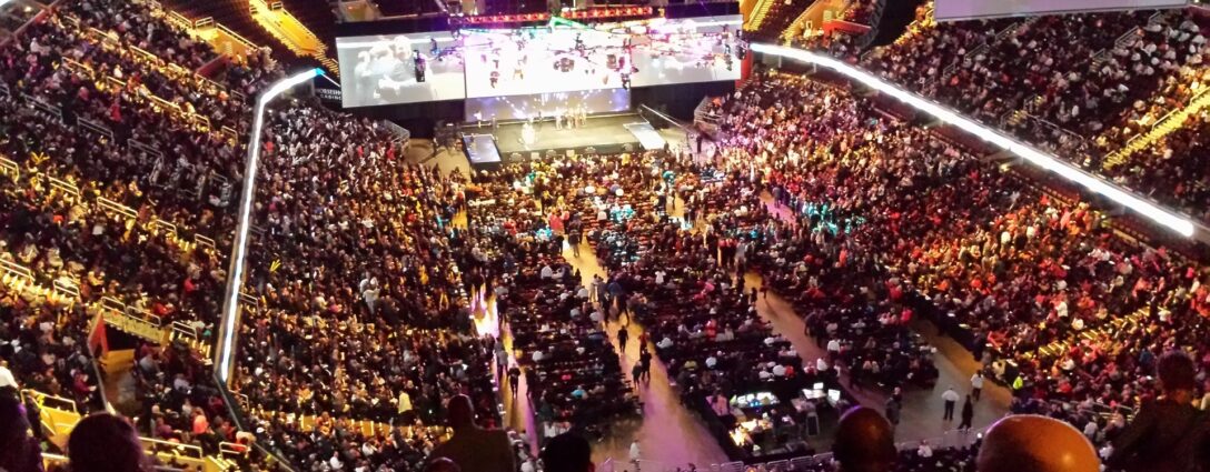 A wide-angle view of a full indoor arena with a stage and large screens in the center demonstrating how Prismm can help create immersive experiences for any venue — before the event even begins.