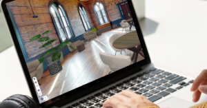 A woman working on her laptop plans an event using a digital twin. She has a camera on her desk near an outdoor environment.